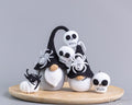 A set of handmade crocheted Halloween gnomes and spider decorations displayed on a round wooden tray against a neutral gray background. The set includes three gnomes with black pointed hats, white beards, and skull faces, along with two black spiders and a small white skull.