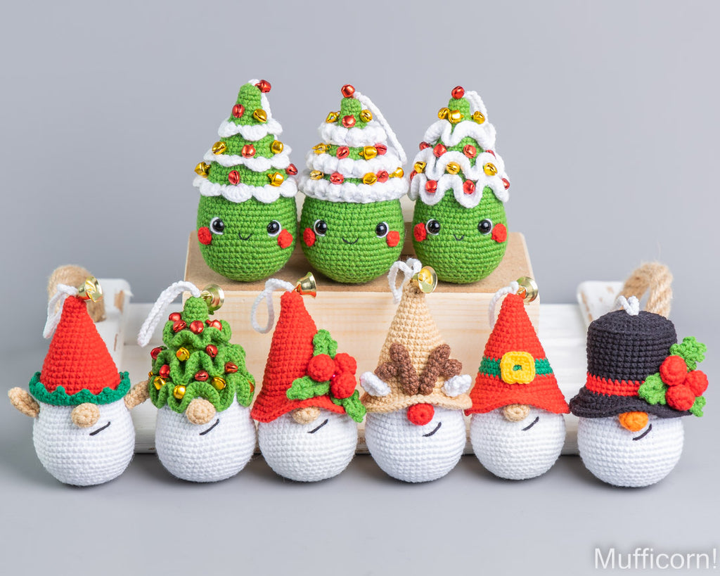 A set of handmade crocheted Christmas-themed plush ornaments, including three decorated Christmas trees on a wooden block and five snowmen with various festive hats, arranged against a neutral gray background.