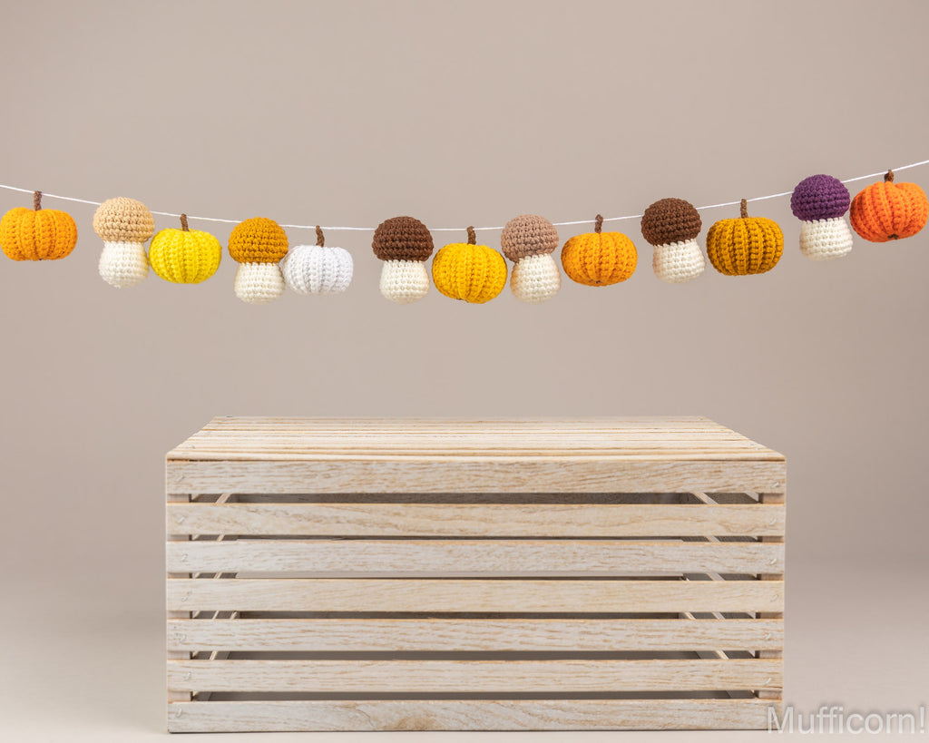 A string of crocheted pumpkin garland ornaments in orange, yellow, white, brown, and purple, displayed above a light wood slat crate on a neutral beige background.