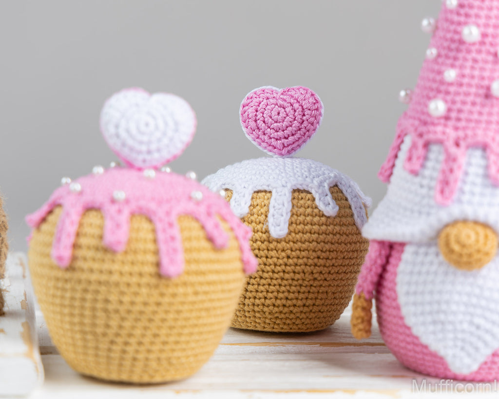 Three crocheted plush toys shaped like cupcakes and a gnome, displayed on a light wooden surface against a soft gray background.