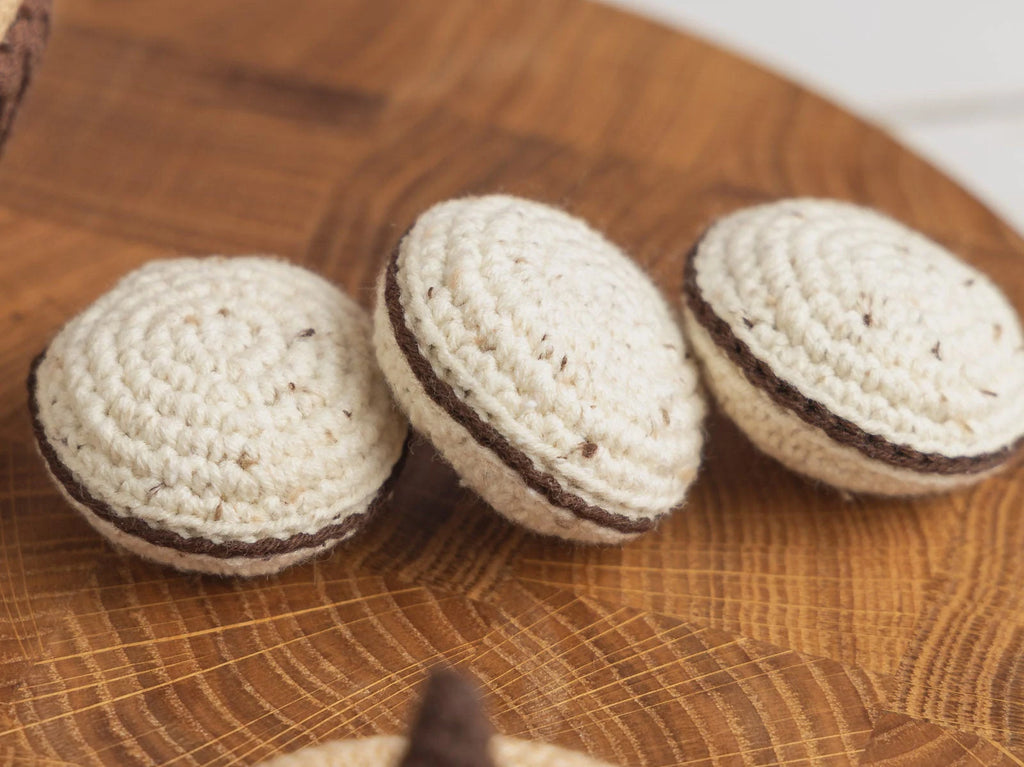 Three small crocheted cream-colored items with dark brown bands, arranged on a round wooden surface.