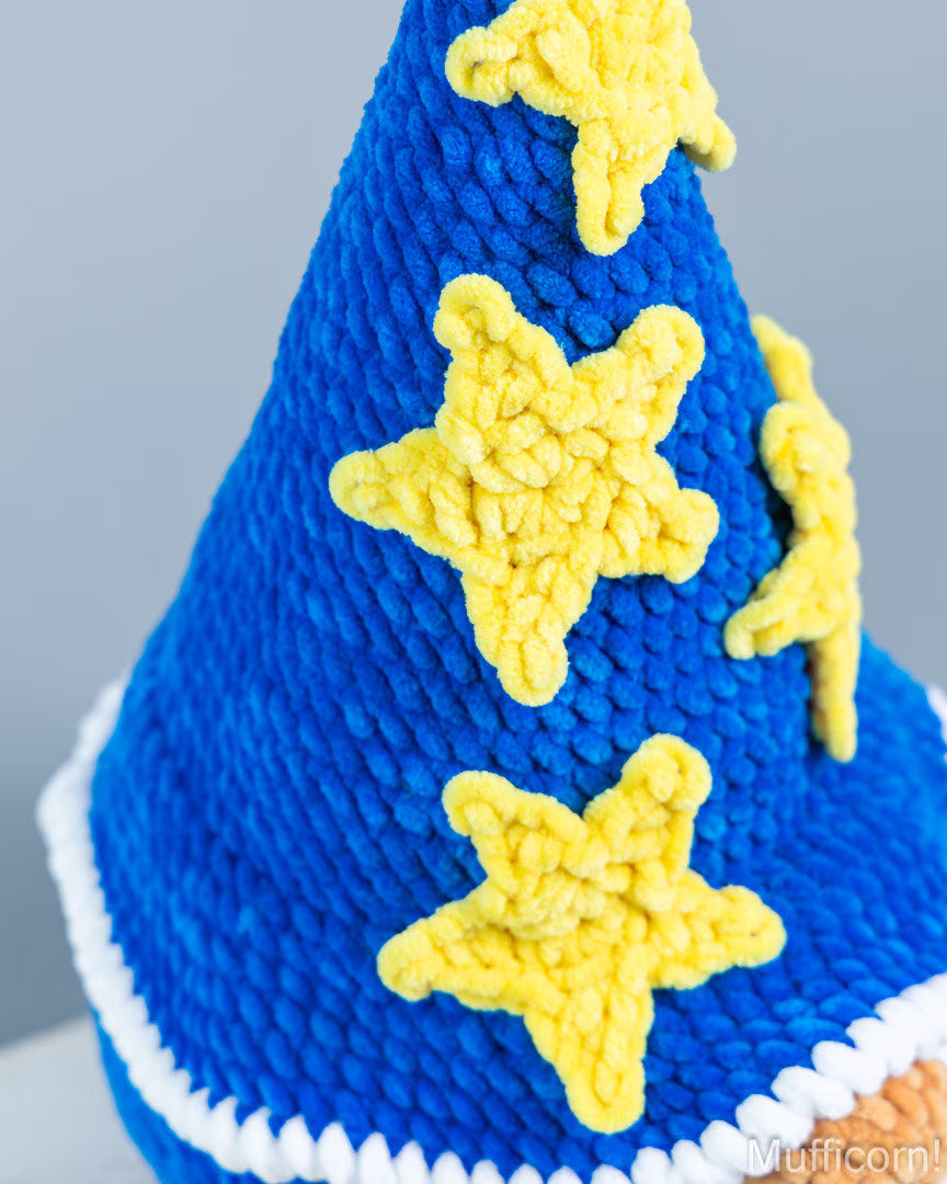 Close-up of a blue textured party hat with yellow star appliqués and a white piped edge, photographed against a light gray background.