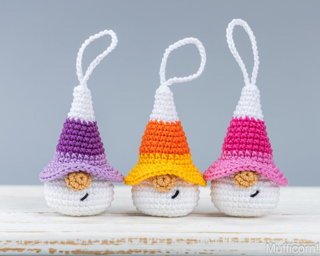 Three crocheted Halloween gnomes keychains, shaped like candy corns in three different colors