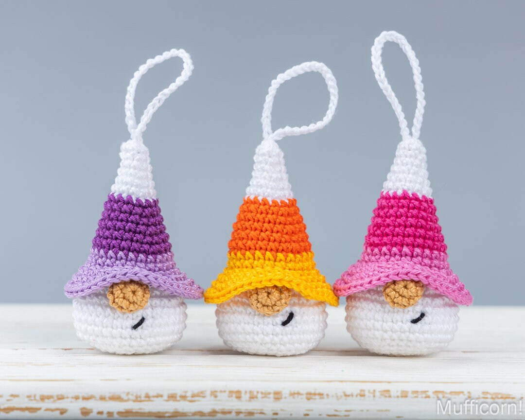 Three crocheted Halloween gnomes keychains, shaped like candy corns in three different colors