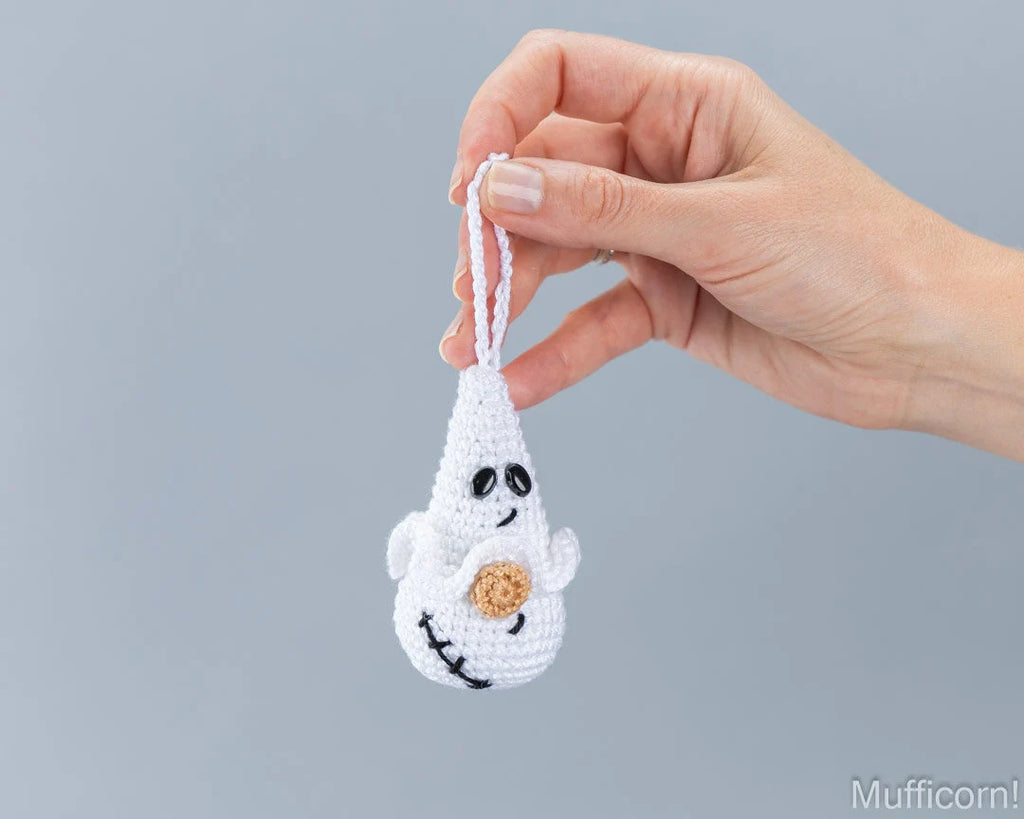 A hand holding a small white crocheted ghost ornament with black embroidered scar