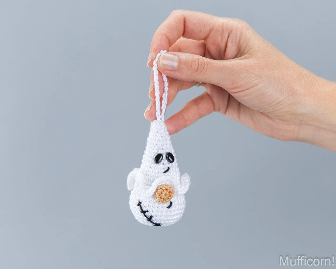 A hand holding a small white crocheted ghost ornament with black embroidered scar