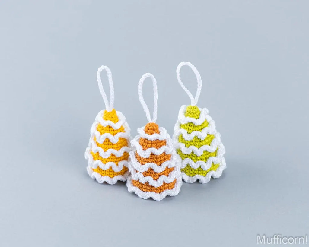 Three small crocheted christmas tree ornament pendants on a light gray background, featuring yellow and white, orange and white, and lime green and white patterns.