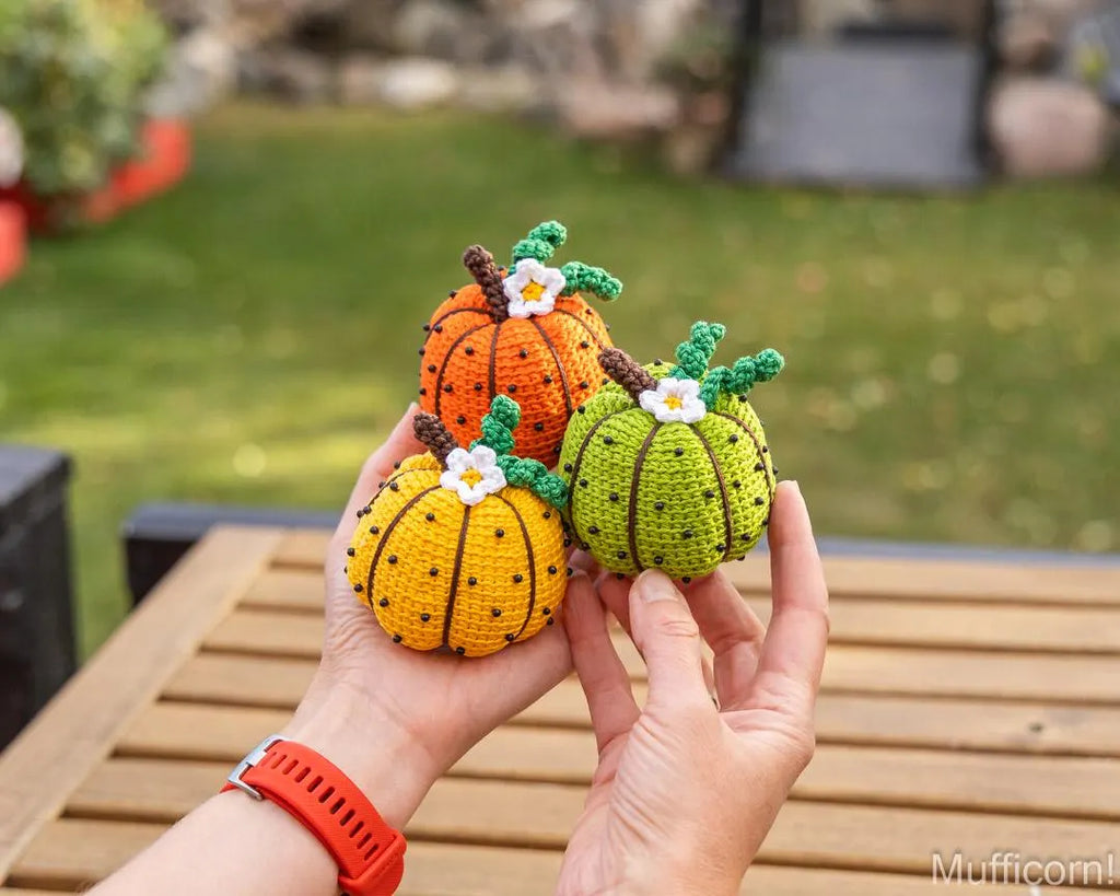 Orange, green and yellow crochet pumpkins held in hand