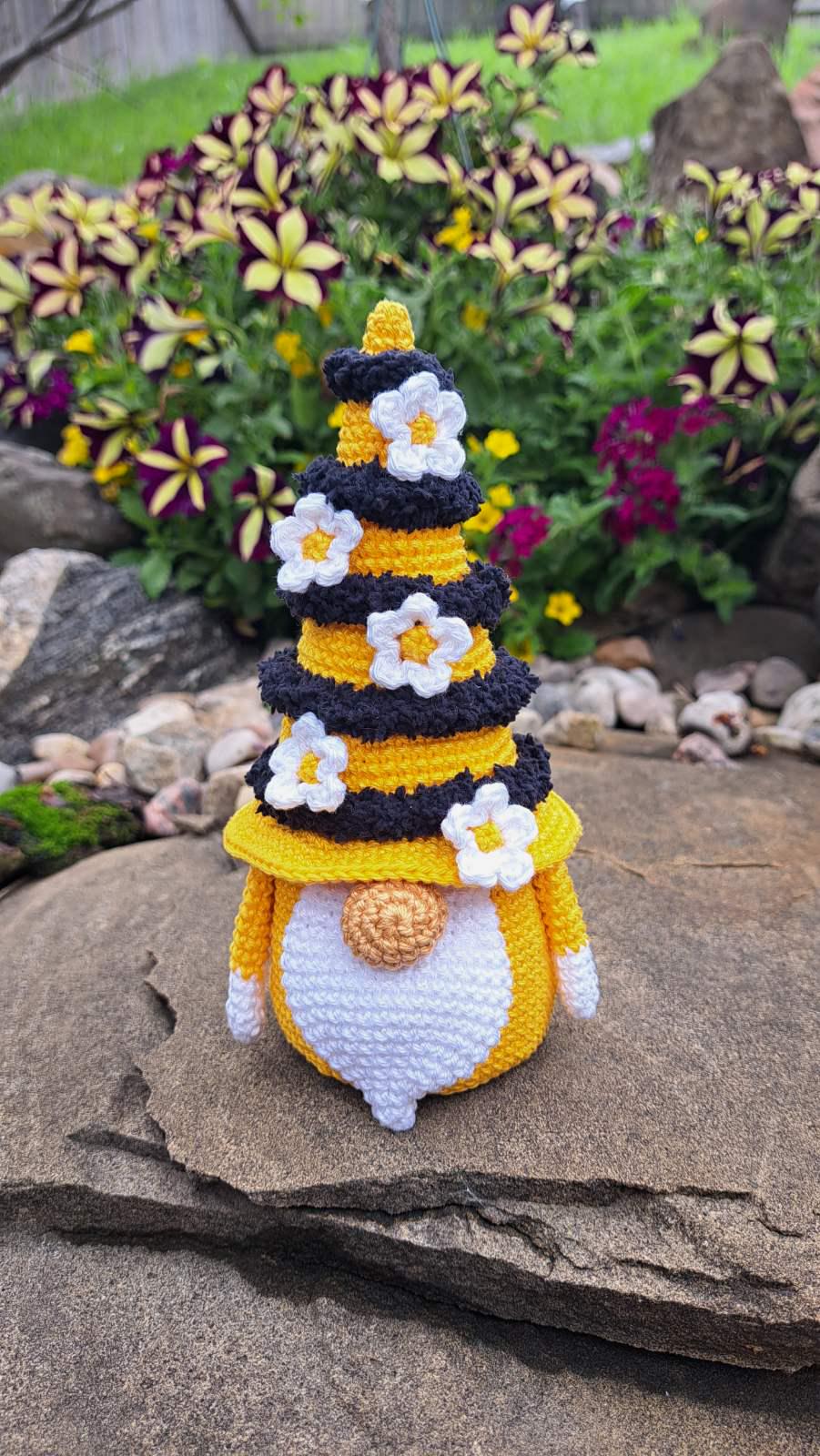 Crochet bee gnome candy keeper sitting on rock in garden