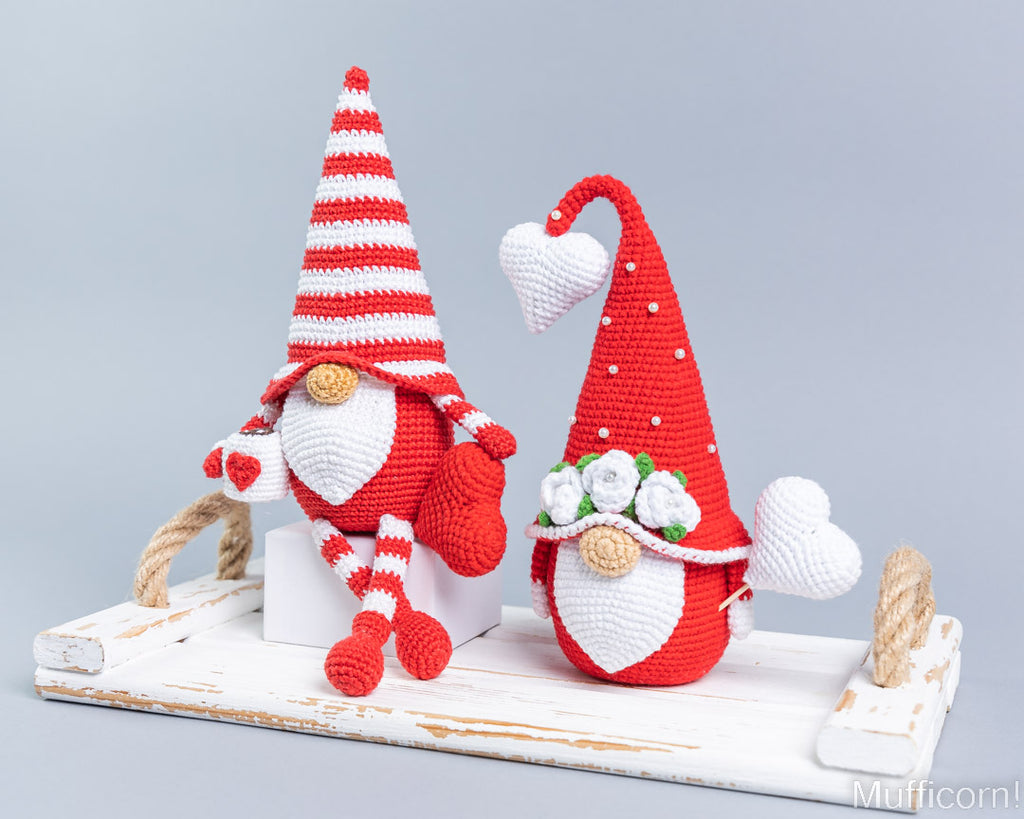 Two crocheted Valentine gnomes in red and white, displayed on a distressed white wooden tray against a light gray background.