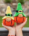 Two crocheted gnome pumpkins held in hands outdoors. One has a yellow hat with a green buckle and the other has a green hat with a yellow buckle.