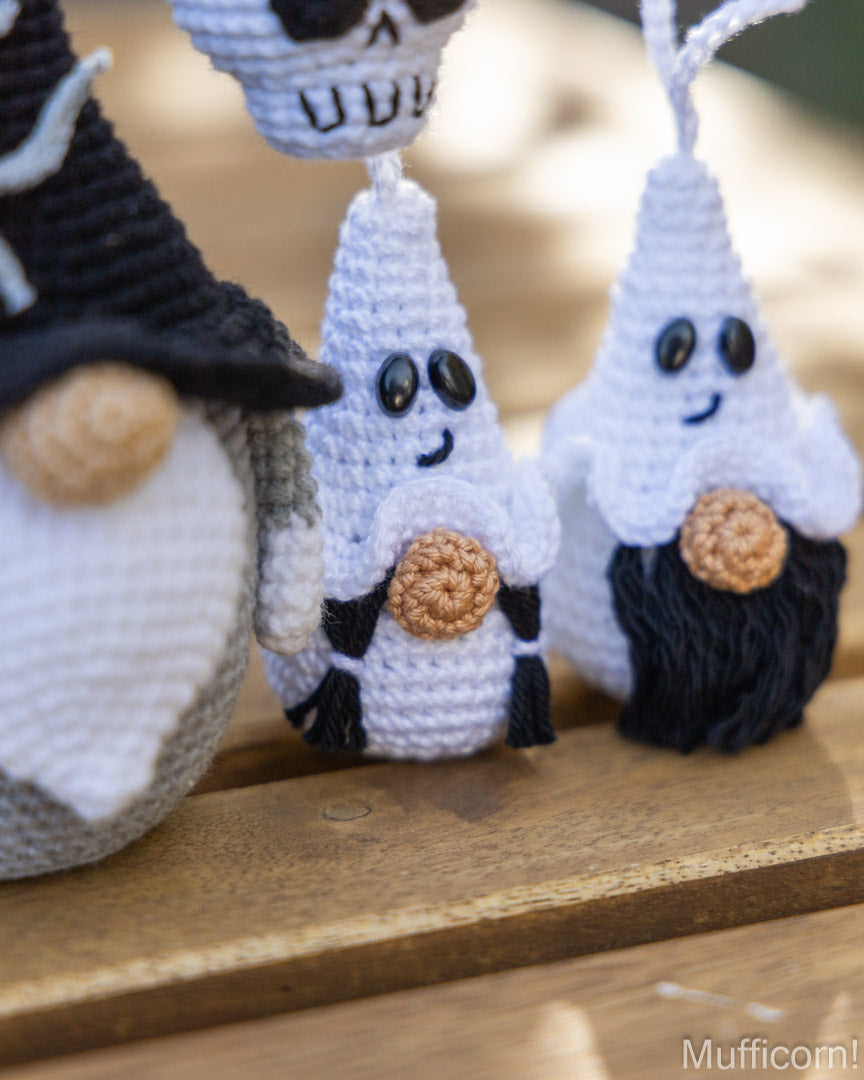 Three crocheted ghost ornaments with embroidered faces and small brown buttons, displayed on a wooden surface outdoors.