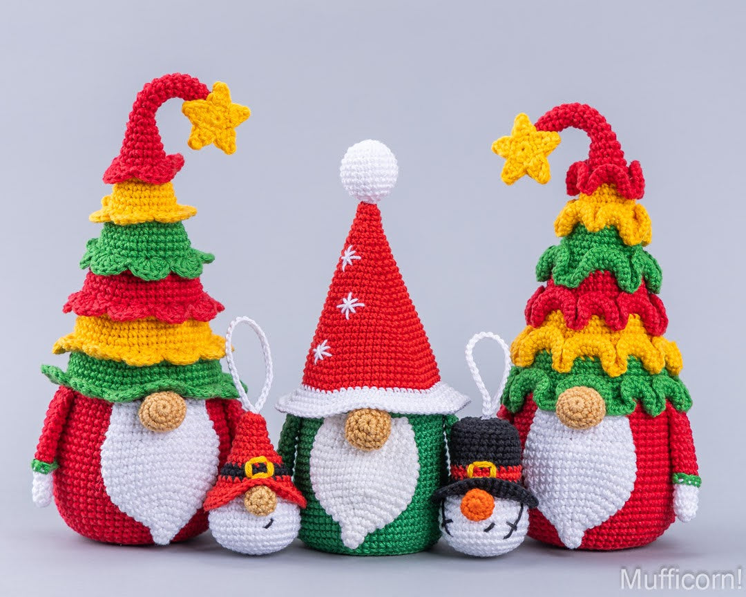 Four crocheted Christmas gnomes arranged against a light gray studio background. The set includes two tall gnomes with Christmas tree hats in red, yellow, and green, one central gnome in a red Santa hat, and one small black-and-white snowman gnome.