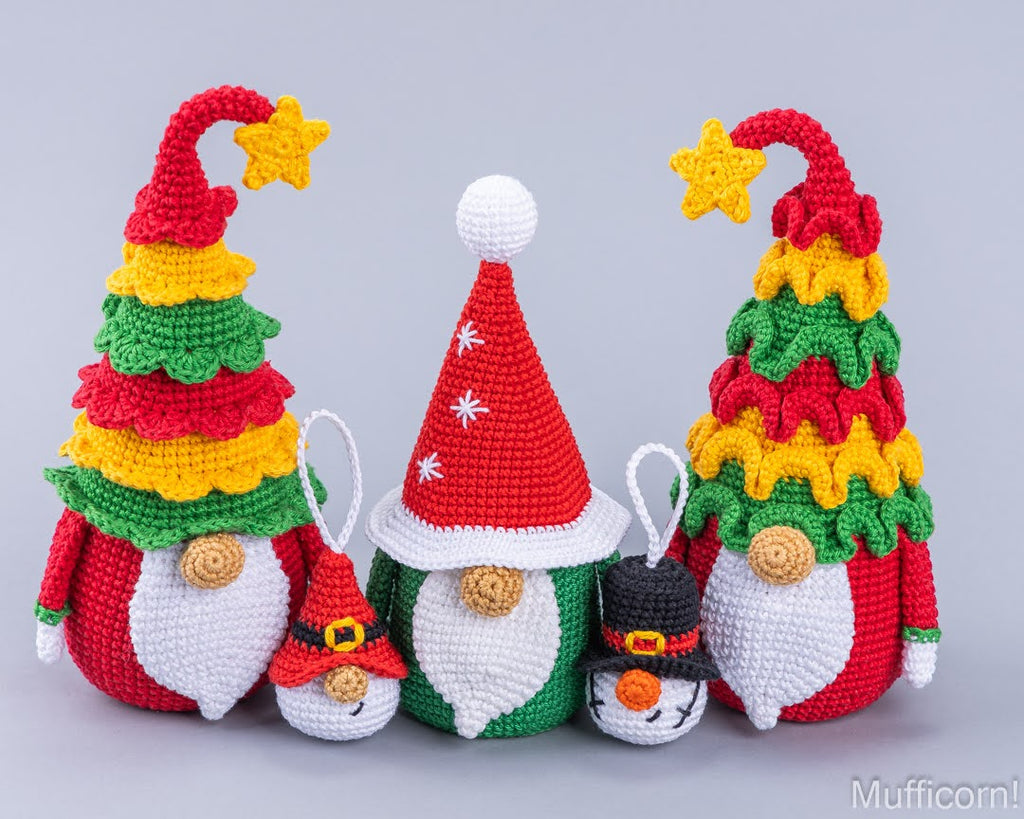 Four crocheted Christmas gnomes in different sizes, featuring colorful tree-shaped hats in red, yellow, and green, white beards, and festive accessories, displayed against a solid gray background.