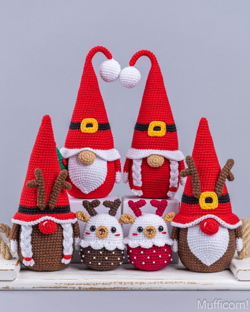 A set of five crocheted Christmas gnomes and reindeer dolls arranged on a white wooden surface against a light gray background. The collection includes three gnome figures in red hats with white beards, two small white-and-brown gnomes, and two reindeer figures in red and brown hats.