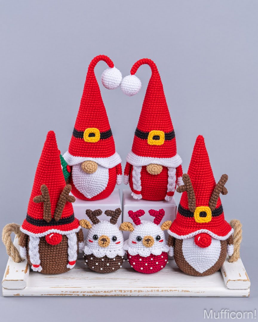 A set of five crocheted Christmas-themed gnomes and reindeer dolls arranged on a white wooden tray against a solid gray background. The set includes two Santa Claus figures, two reindeer, and one small white and red bird gnome, all featuring red hats, white trim, and colorful accents.
