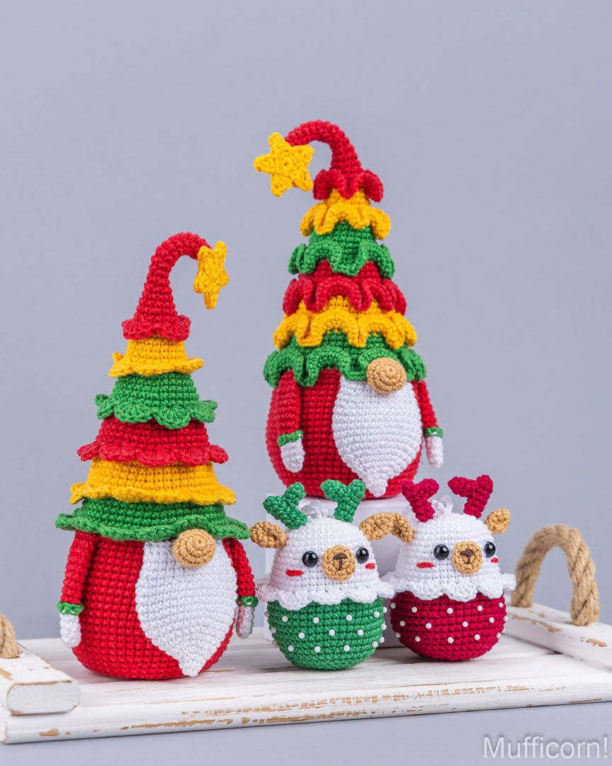 Three crocheted Christmas gnomes with colorful tree-shaped hats and white beards, displayed on a white wooden surface against a light gray background.