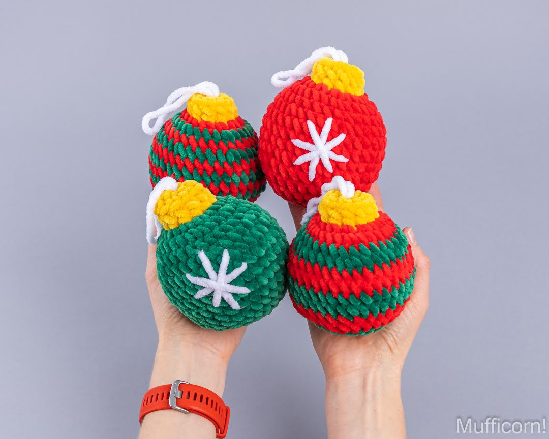 Four crocheted Christmas ornament balls held in two hands against a solid gray background. The ornaments are made of textured yarn in red, green, yellow, and white, with some featuring white starburst patterns.