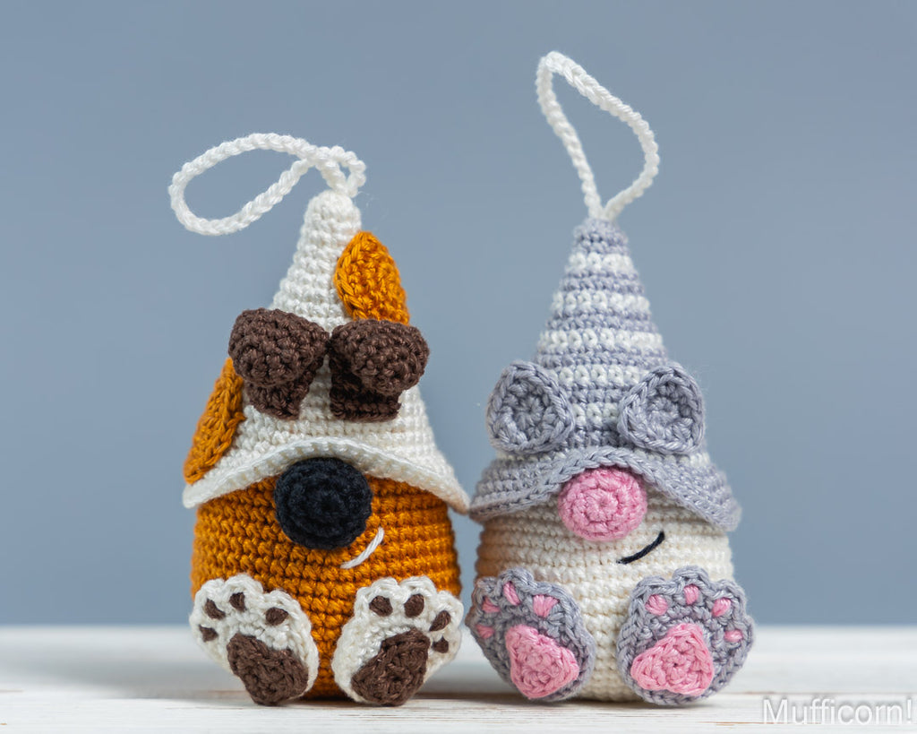 Two crocheted hanging ornaments shaped like a dog and a gnome, displayed side by side against a soft blue-gray background.
