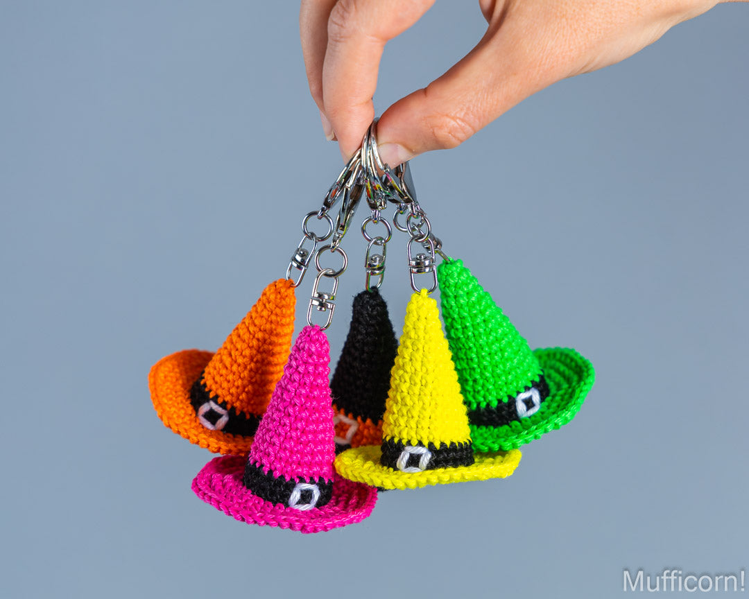 Colorful crochet witch hat keychains in green, orange, pink, yellow and black hanging in hand