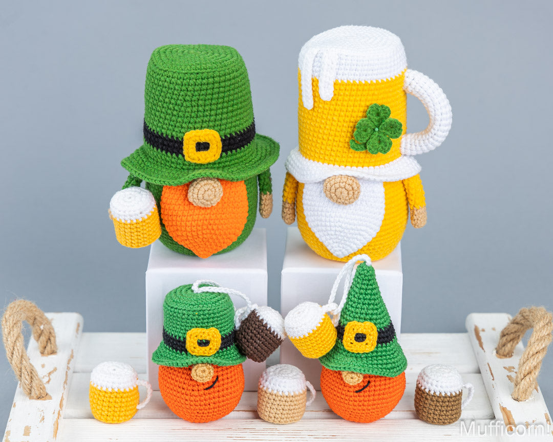 Four crocheted leprechaun gnome figures styled with St. Patrick's Day themes, including hats, beards, and beer mugs, displayed on white pedestals against a gray background.